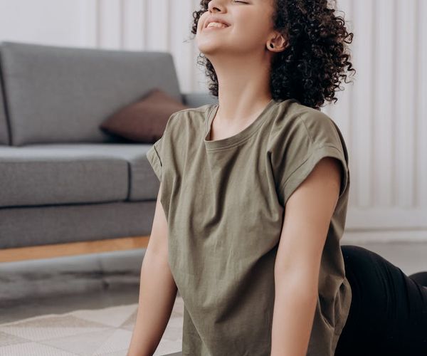 Smiling pregnant woman meditating peacefully on a yoga mat near a window.
